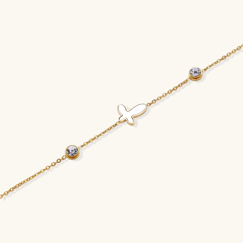 Gold chain bracelet with white mother of pearl butterfly pendant and two bezel-set crystals on cream background